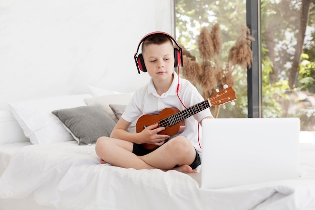 Bezpłatne zdjęcie chłopiec z hełmofonami bawić się ukulele