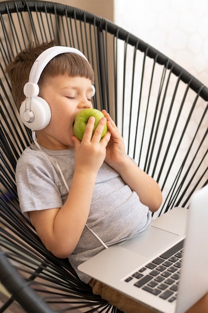 Bezpłatne zdjęcie chłopiec z hełmofonami i laptopem cieszy się jabłka