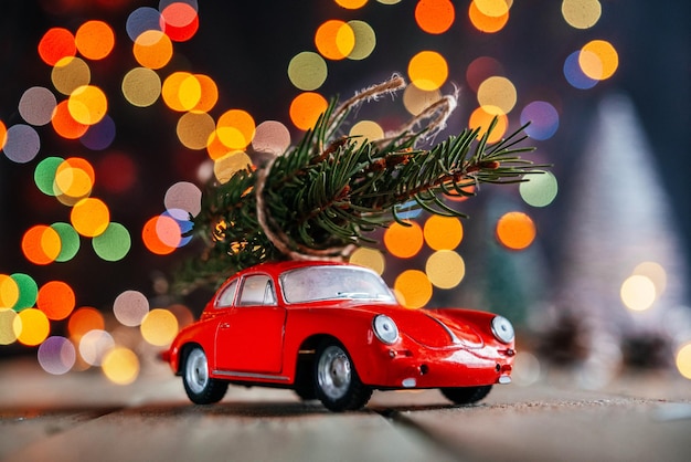 Choinki dostawy tło czerwony samochodzik z jodły na kolorowe bożonarodzeniowe światła bokeh