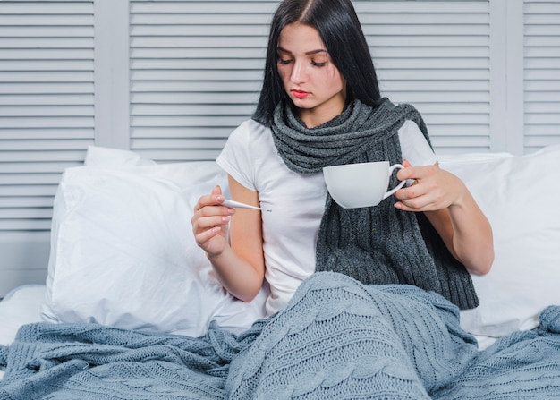 Chora kobieta trzyma filiżankę kawy patrzeje termometr