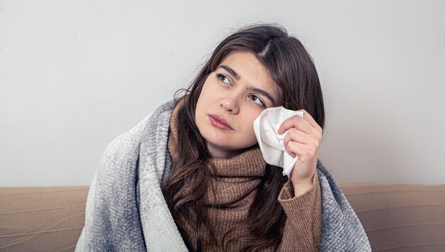 Chora młoda kobieta w domu na kanapie z przeziębieniem