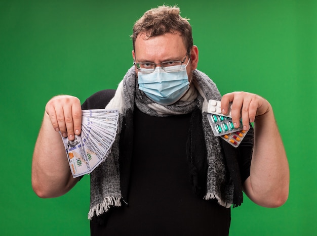 Chory mężczyzna w średnim wieku noszący maskę medyczną i szalik na zielonej ścianie