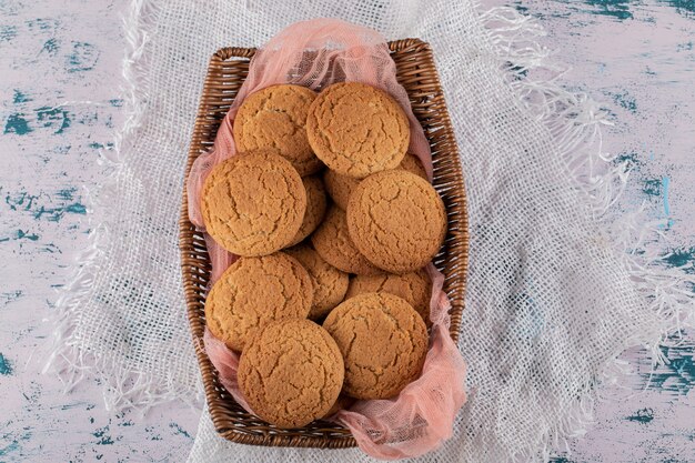 Ciasteczka owsiane w drewnianym koszu na różowym ręczniku kuchennym.