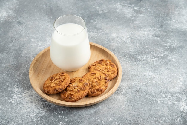 Ciasteczka z ekologicznymi orzeszkami ziemnymi i szklanką mleka na drewnianym talerzu.