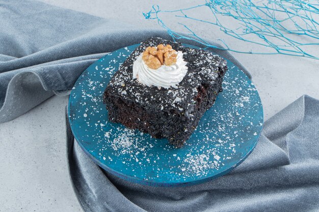 Ciasto czekoladowe pokryte proszkiem waniliowym na małej desce na tle marmuru.