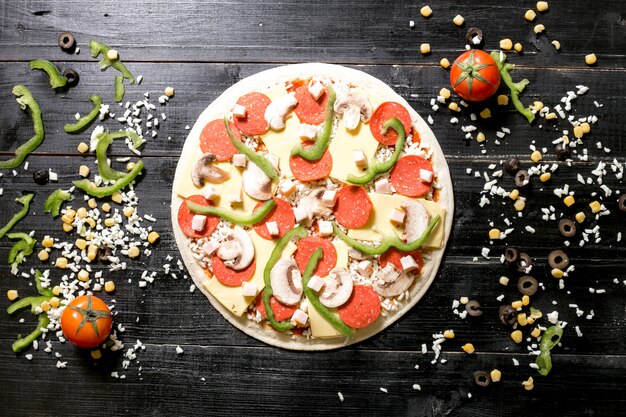 Ciasto do pizzy z serem borowikowym na wierzchu obok sera posypuje oliwkowym pomidorem kukurydzianym
