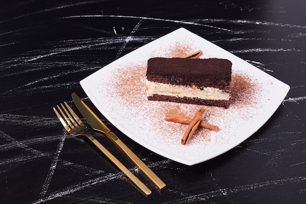 Bezpłatne zdjęcie ciasto tiramisu z cynamonem na białym talerzu obok złotych sztućców.