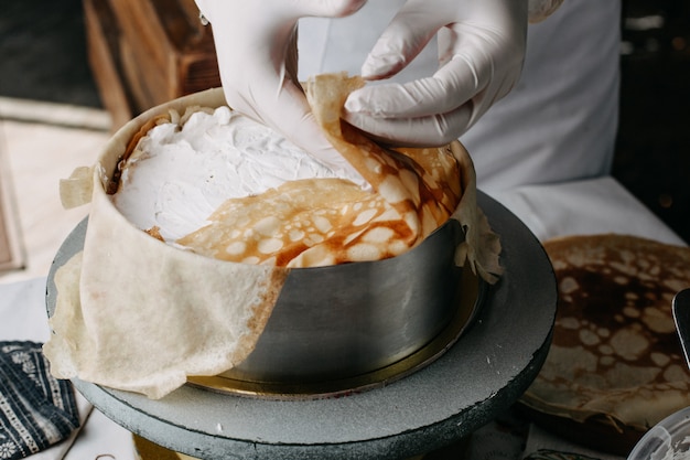 ciasto w okrągłej patelni z kucharzem rozprowadzającym na nim kwaśną śmietanę w kuchni