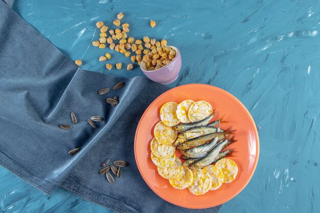 Ciecierzyca, nasiona obok suszonego szprota i chipsów serowych na talerzu na ręczniku, na niebieskiej powierzchni.