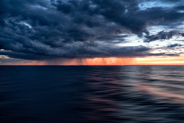 Ciemne chmury zachodzącego słońca nad ciemną wodą oceanu