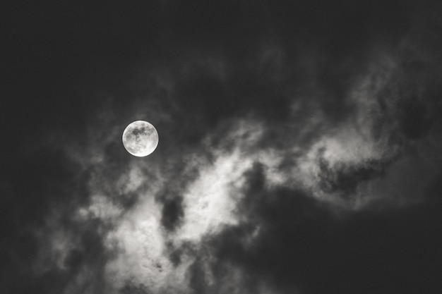 Ciemne ujęcie pełni księżyca rozpościerającego światło za chmurami w nocy