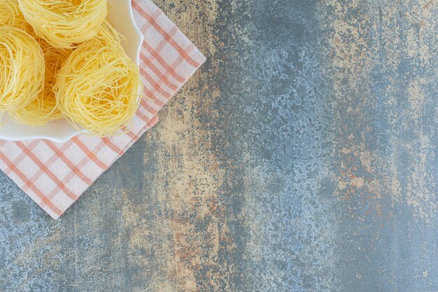 Bezpłatne zdjęcie cienkie spaghetti w misce na ręczniku, na marmurowym tle.