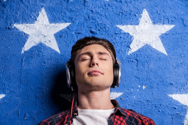 Cieszyć się muzyką. niski kąt widzenia młodego mężczyzny w słuchawkach, który ma zamknięte oczy, stojąc na tle
