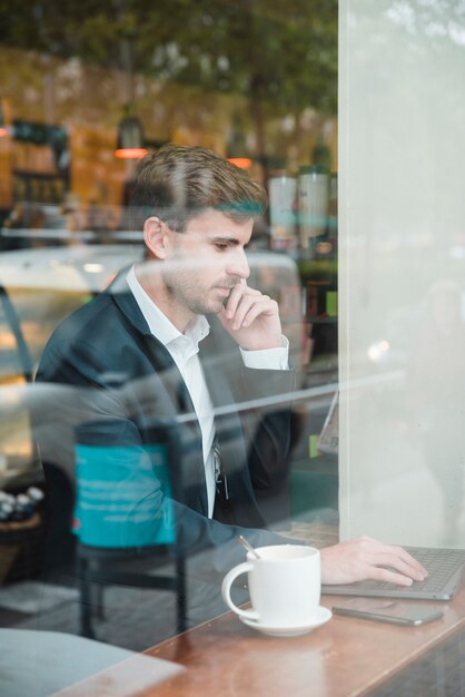 Close-up biznesmena za pomocą laptopa biorąc na telefon komórkowy w kawiarni