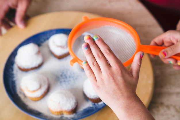 Bezpłatne zdjęcie close-up dziewczyna spryskiwanie cukru na cupcakes