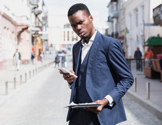 Close-up młodego biznesmena gospodarstwa schowka w ręku przy użyciu telefonu komórkowego