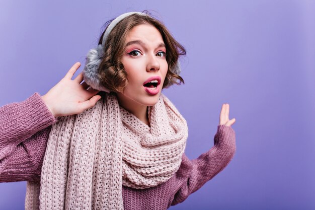 Close-up portret beztroskiej kobiety kręcone z ładną buzią pozowanie w szalik z dzianiny. Ciemnowłosa niesamowita dama w swetrze stojąca na fioletowej ścianie.