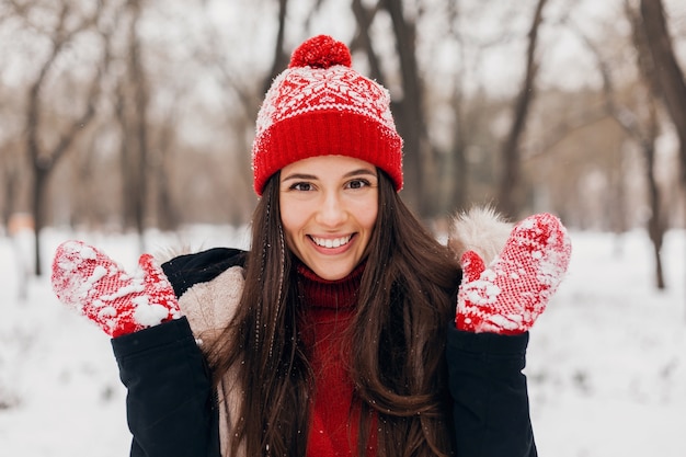Close-up portret młodej całkiem uśmiechniętej szczęśliwej kobiety w czerwonych rękawiczkach i czapce na sobie zimowy płaszcz, spacery w parku w śniegu, ciepłe ubrania
