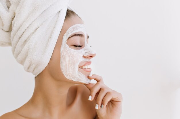 Close-up portret pięknej młodej kobiety uśmiechając się z ręcznikami po kąpieli zrobić maseczkę kosmetyczną na jej twarzy.