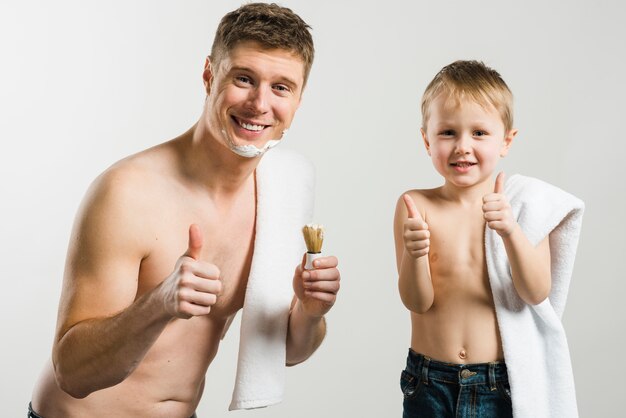 Close-up shirtless młody człowiek i chłopiec z białym ręcznikiem na ramieniu pokazano kciuk znak