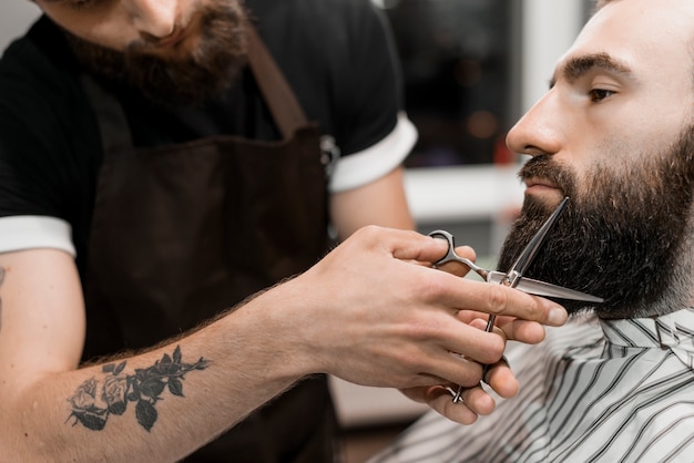 Close-up z ręki do fryzjera cięcia brody mężczyzny z nożyczkami