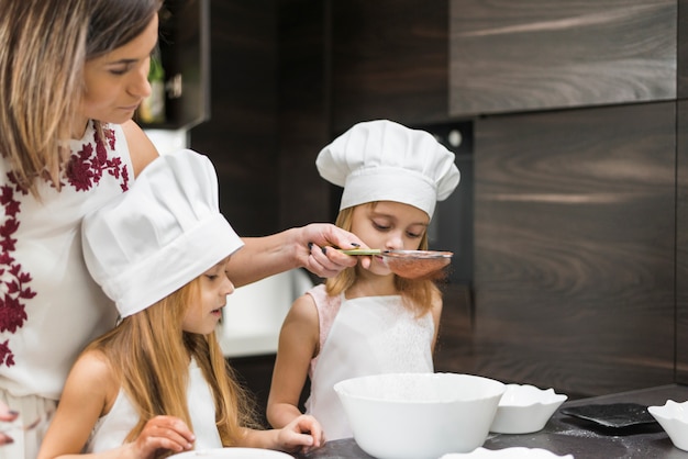 Córki patrzeje matki odsiewa kakaowego proszek przez durszlaka w kuchni