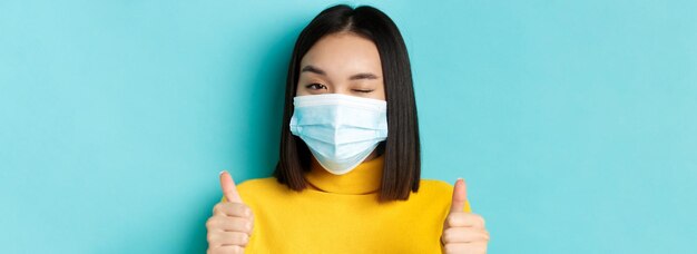 Covid dystans społeczny i koncepcja pandemii urocza azjatycka dziewczyna w masce medycznej mrugająca do kamery