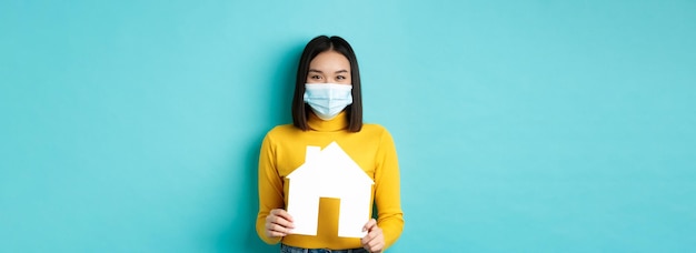 Bezpłatne zdjęcie covid pandemia i koncepcja nieruchomości wesoła azjatycka kobieta uśmiechająca się w masce medycznej pokazująca papier ho