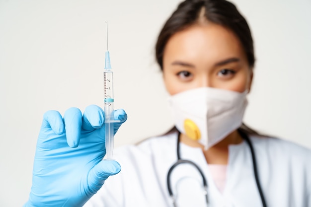Bezpłatne zdjęcie covid szczepienia i koncepcja kwarantanny azjatycka kobieta lekarz na twarzy respirator pokazujący wypełnienie strzykawki...
