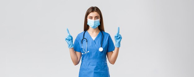 Covid19 zapobieganie wirusowi zdrowie pracowników opieki zdrowotnej koncepcja Poważna i pewna siebie pielęgniarka w niebieskiej masce medycznej ŚOI wskazujące palce w górę informują pacjentów, jak zapobiegać infekcji koronowej