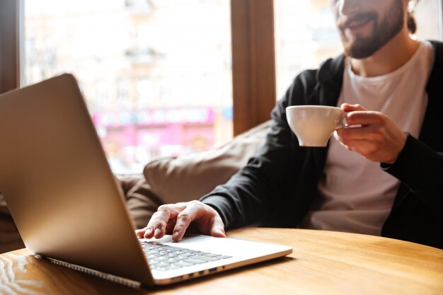 Cropped wizerunek Brodaty mężczyzna używa laptop w kawiarni