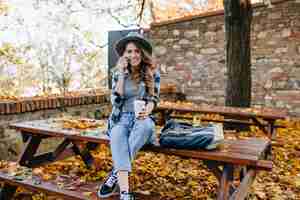 Bezpłatne zdjęcie cudowna szczupła dama nosi krótkie dżinsy, siedząc na stole ze skrzyżowanymi nogami w jesienny dzień