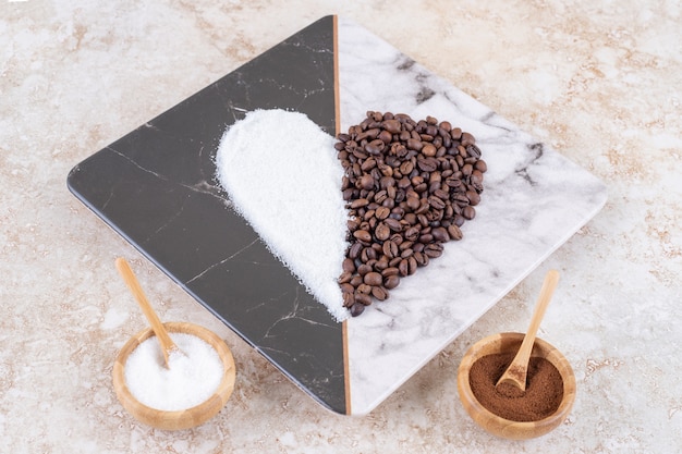 Bezpłatne zdjęcie cukier i ziarna kawy w małych miseczkach i ułożone w kształcie serca na marmurowym talerzu