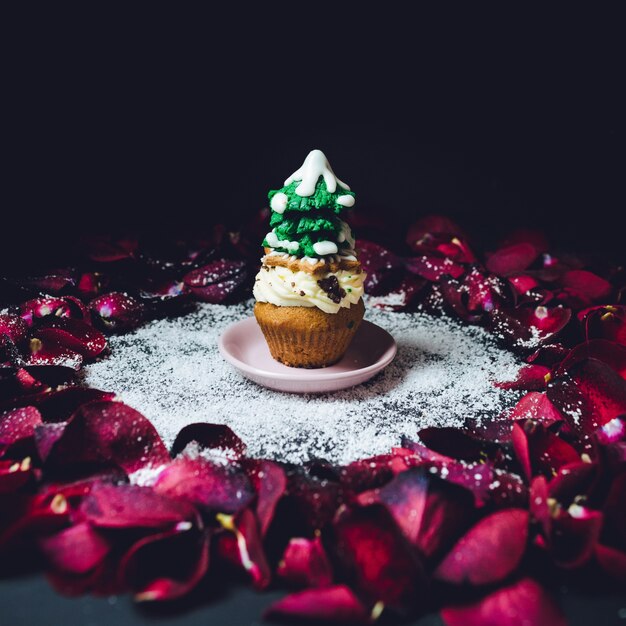 Cupcake z glazurą jodła na górze stoi w kręgu płatków róży