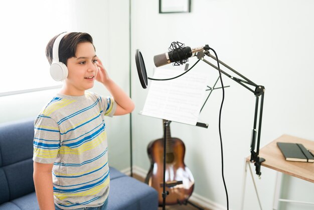 Ćwiczę na lekcjach muzyki. Śliczny szczęśliwy chłopiec nagrywa piosenkę z mikrofonem na lekcje śpiewu