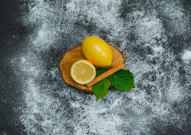 Cytryny z wysokim kątem widzenia z liśćmi i suchym cynamonem na kawałku drewna i ciemności. poziomy