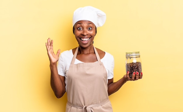 Czarna afro szefowa kuchni czuje się szczęśliwa, podekscytowana, zaskoczona lub zszokowana, uśmiechnięta i zdumiona czymś niewiarygodnym. koncepcja ziaren kawy