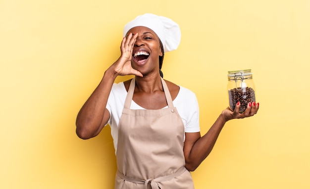 Czarna Kobieta Szefa Kuchni Afro Czuje Się Szczęśliwa, Podekscytowana I Pozytywna, Wydając Wielki Okrzyk Z Rękami Przy Ustach, Wołając. Koncepcja Ziaren Kawy Premium Zdjęcia