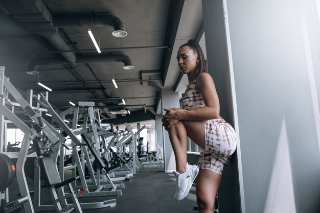 Czarna kobieta w świetnej wysportowanej sylwetce rozgrzewa mięśnie przed ćwiczeniem na sprzęcie sportowym