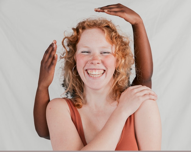 Czarna skóra kobiety ręka za uśmiechniętym caucasian żeńskim przyjacielem przeciw popielatemu tłu