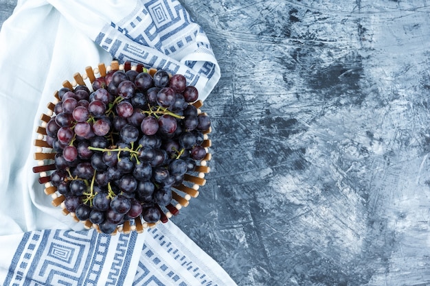 Bezpłatne zdjęcie czarne winogrona w koszu leżały na nieczysty tynk i tło ręcznik kuchenny