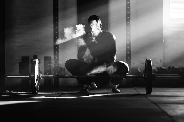 Czarno-białe zdjęcie umięśnionego mężczyzny używającego kredy sportowej przed podniesieniem sztangi podczas treningu siłowego na siłowni