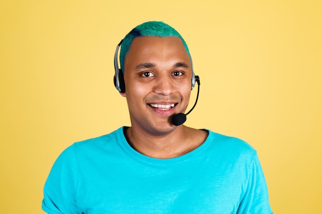 Czarny afrykański mężczyzna dorywczo na żółtej ścianie niebieskie włosy pracownik call center szczęśliwy operator obsługi klienta ze słuchawkami