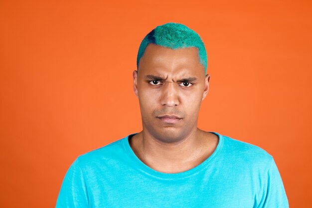 Czarny afrykański mężczyzna w swobodnym ubraniu na pomarańczowej ścianie niebieskie włosy marszczy brwi nie zgadza się rozczarowany poważny