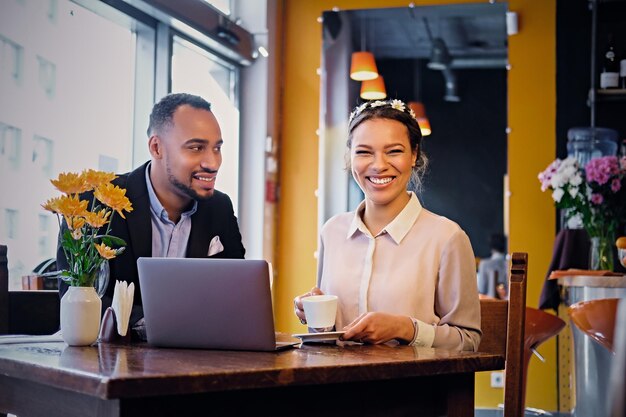 Czarny biznes Afroamerykanin mężczyzna i kobieta pije kawę i korzysta z laptopa w restauracji.