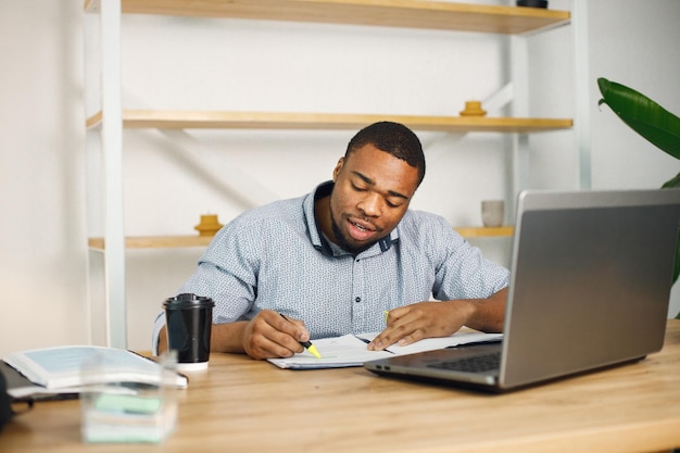 Czarny mężczyzna przedsiębiorca siedzi w biurze za pomocą laptopa i pisze notatki
