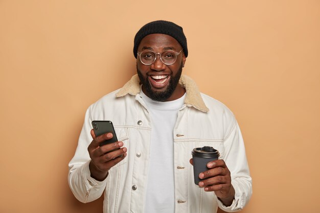 Czarny, nieogolony dorosły mężczyzna w stylowym stroju, korzysta z nowoczesnego smartfona do rozmów online