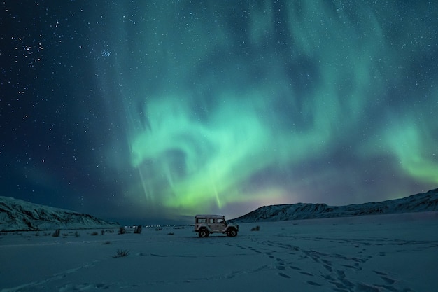 Czarny SUV na zaśnieżonym polu pod zielonymi światłami zorzy polarnej