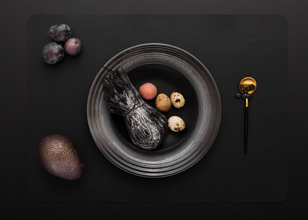 Czarny talerz z czarnym makaronem i przepiórek jajkami na ciemnym tle