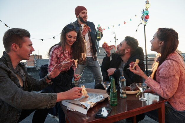 Czas na śpiewanie Tak przynajmniej myśli facet w czerwonym kapeluszu. Jedzenie pizzy na imprezie na dachu. Dobrzy przyjaciele mają weekend z pysznym jedzeniem i alkoholem